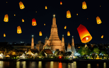 Ribuan krathong bercahaya lilin mengapung di sungai di bawah langit malam yang diterangi bulan purnama, dengan lentera langit melayang di kejauhan, mencerminkan suasana magis Festival Loy Krathong di Thailand