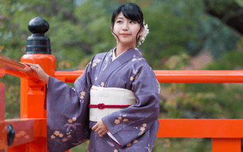Wisatawan mengenakan kimono berfoto dengan latar bunga sakura di Kyoto.